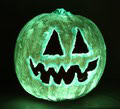 A Halloween pumpkin with triangular eyes and a jagged mouth glows with a green light in the dark.